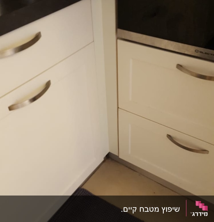 ארונות מטבח לבנים עם ידיות מתכת, בקבוק שמן על השיש